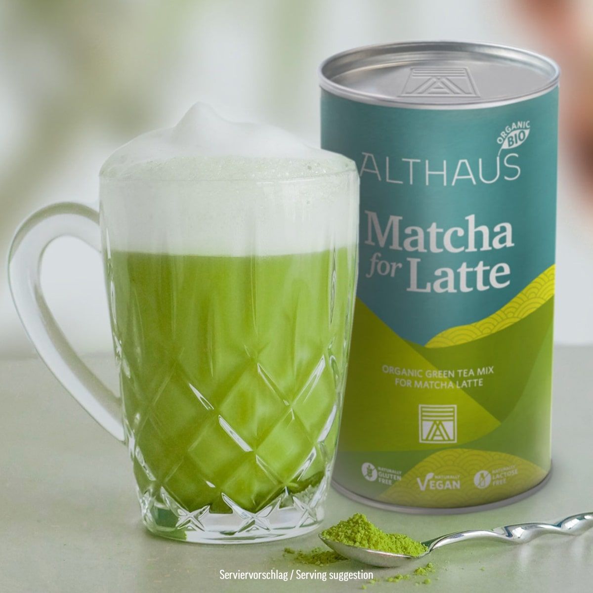 Matcha green tea latte in a glass mug with a can of Althaus Matcha for Latte on a light background