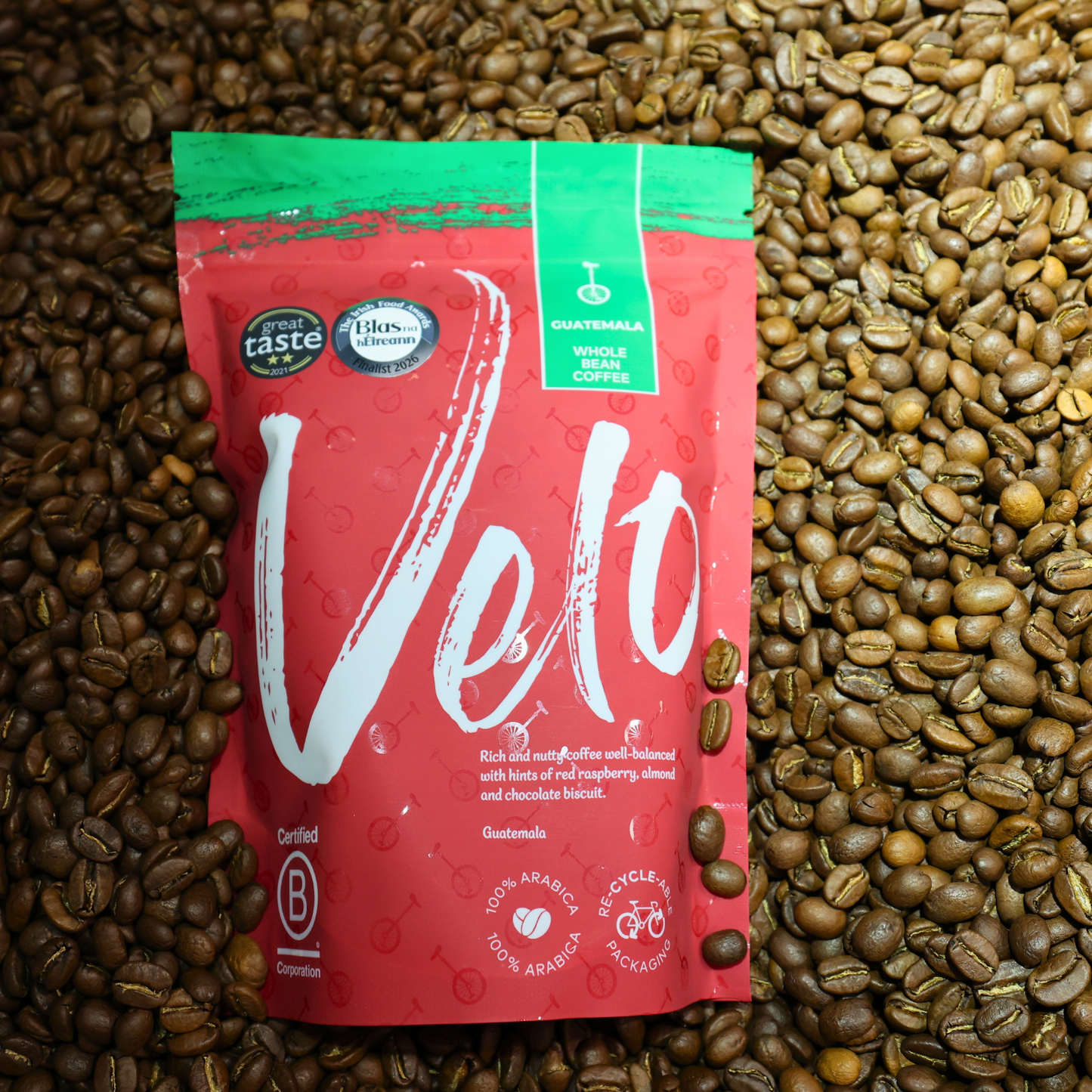 A red and green Velt whole bean coffee pouch from Guatemala, surrounded by a dense background of roasted coffee beans.